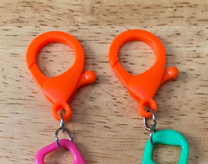 May include: Two orange plastic clasps with silver metal rings attached to pink and green plastic loops.