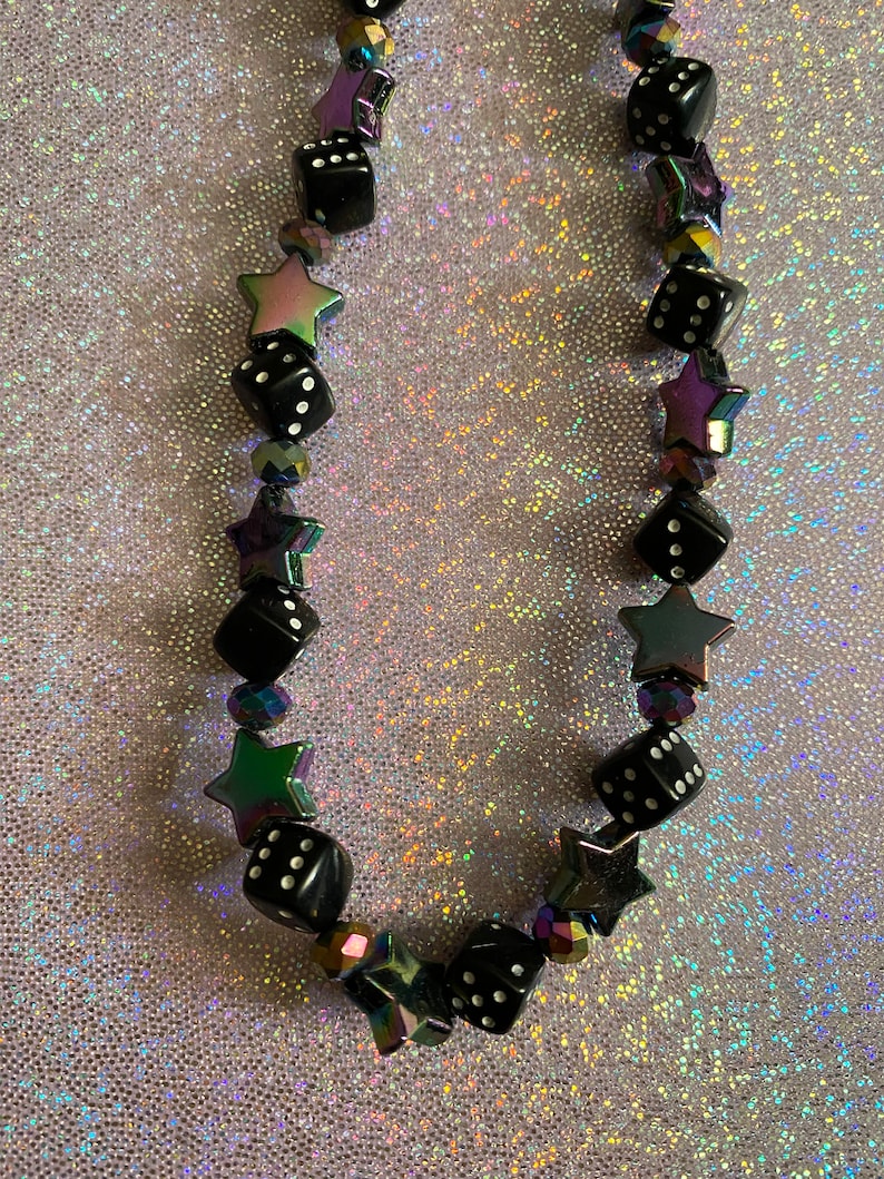 May include: A black and iridescent necklace with black dice and star-shaped beads.