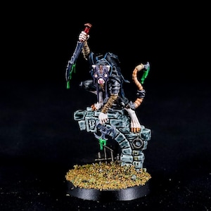 Puede incluir: Figura en miniatura de una criatura parecida a una rata, posando sobre una estructura de piedra. La figura está pintada con armadura detallada, una cola y una daga levantada. Acentos verdes y una base negra completan el diseño.