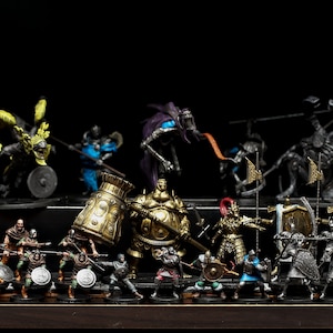 May include: A collection of painted miniature figures, including a large golden warrior with a giant hammer, a winged demon, and a group of armoured soldiers. The figures are arranged on a black surface and appear to be part of a tabletop game or role-playing game.