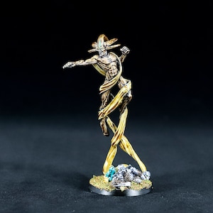 Op de afbeelding: Een geschilderd miniatuurbeeldje van een humanoïde figuur met een skeletachtige verschijning, omhuld door wervelende gouden linten. De figuur is geposeerd in een dynamische houding met één arm uitgestrekt en de andere gebald tot een vuist. Het miniatuur staat op een ronde basis met een getextureerd oppervlak en groene en grijze accenten.