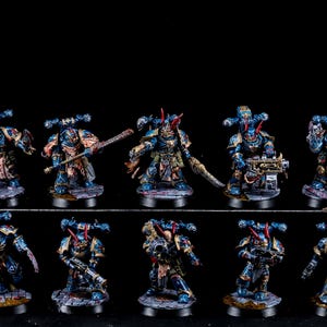May include: A collection of miniature figures, each painted in shades of blue, gold, and red. The figures are detailed with weapons and armor, and are set on textured bases. The figures are arranged in two rows against a black background.