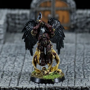 May include: A miniature figure of a winged warrior in red and black armour, holding a sword. The figure is standing on a base with a skull and scroll design.