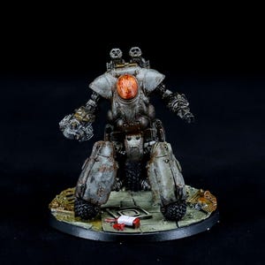 Pode incluir: Um modelo em miniatura de robô cinza e marrom desgastado, com uma cabeça laranja. O robô tem braços e pernas articulados e é montado em uma base circular. O modelo tem uma aparência desgastada e danificada.