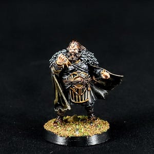 May include: Miniature figurine of a warrior with a long beard, wearing a black and gold outfit with a fur-lined cape. The figure stands on a small, circular base with a grassy texture. The Pike & Dagger logo is in the upper right corner.