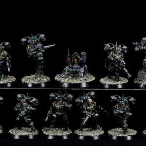 May include: A group of 12 green and gold painted miniature figures, each with a unique pose and weapon, standing on black bases. The figures are part of a tabletop wargame.