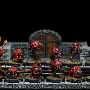 May include: A set of 12 red and green painted miniature figures, including a goblin with a bagpipe, a goblin with a spear, and several red creatures with sharp teeth. The figures are arranged on a stone surface.