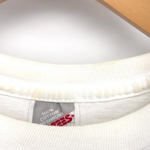 May include: A white t-shirt with a ribbed crew neckline showing signs of light yellow discoloration. A grey fabric tag is sewn into the inner collar, featuring the red text Hanes and the white text 100% Cotton Preshrunk on a grid background.