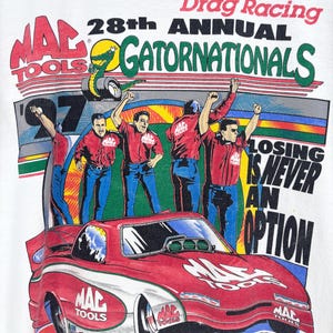 May include: A white t-shirt featuring a graphic for the 28th Annual NHRA Winston Drag Racing Gatornationals. The design includes a red race car, four crew members in red shirts, and the text "Losing is never an option" with Mac Tools branding.