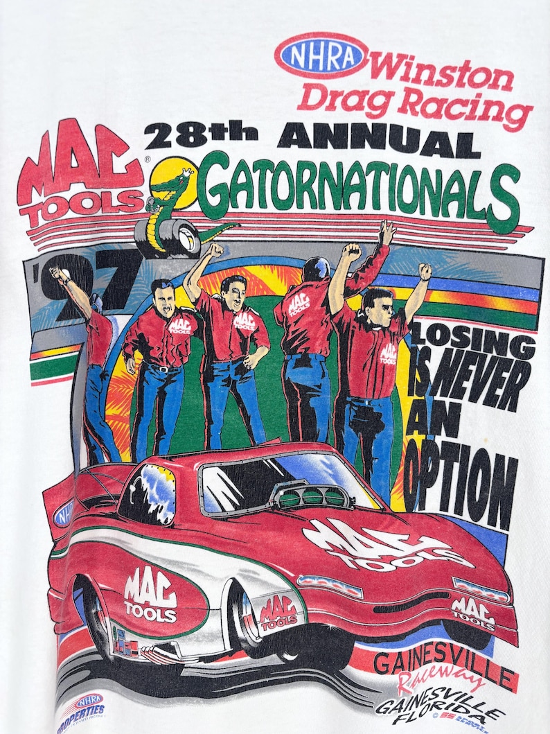 May include: A white t-shirt featuring a graphic for the 28th Annual NHRA Winston Drag Racing Gatornationals. The design includes a red race car, four crew members in red shirts, and the text "Losing is never an option" with Mac Tools branding.