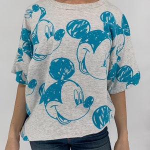 Puede incluir: Una camiseta gris con un estampado azul de Mickey Mouse. El estampado es un estilo de dibujo del rostro de Mickey Mouse.