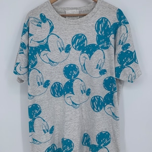 Puede incluir: Una camiseta gris con un estampado azul de Mickey Mouse por todas partes. El estampado de Mickey Mouse es de estilo dibujado.