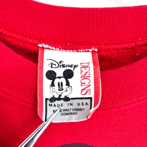 K&ouml;nnte beinhalten: Rotes Sweatshirt mit Mickey Mouse-Grafik. Das Etikett lautet "Disney Designs" und "Made in USA &copy; The Walt Disney Company."
