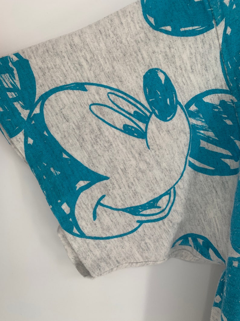 Puede incluir: Camiseta gris con un estampado azul de Mickey Mouse. El estampado es un simple contorno de la cabeza y las orejas de Mickey Mouse.