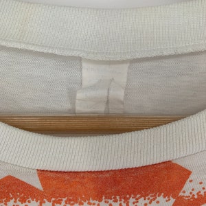 Op de afbeelding: Wit T-shirt met een oranje en witte grafische print. Het shirt heeft een geribbelde ronde hals.