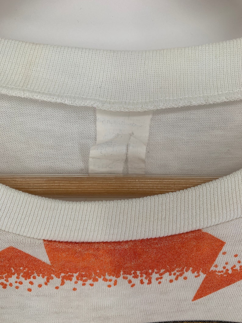 Op de afbeelding: Wit T-shirt met een oranje en witte grafische print. Het shirt heeft een geribbelde ronde hals.
