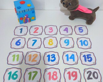 May include: A set of 20 colorful number cards with a decorative border. The numbers are in a playful font and are arranged in a grid pattern. The cards are on a white surface.