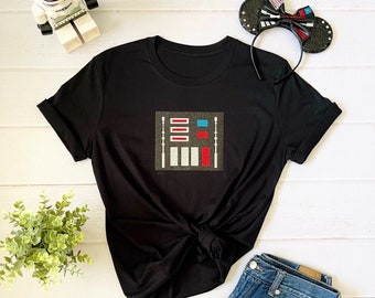 May include: Black t-shirt with a white and red graphic of a control panel from the Star Wars movie franchise. The shirt is paired with denim shorts and a black headband with a red and blue bow.
