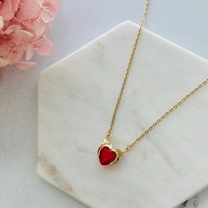 May include: A gold chain necklace with a red heart pendant. The heart has a gold design around the edges.