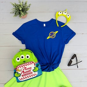 May include: A blue t-shirt with a planet graphic, a green and yellow alien backpack with the text "Pizza Planet", a green and yellow headband with three eyes, a pair of black sunglasses, and a pair of white sneakers.