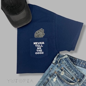 May include: A navy blue t-shirt with a pocket featuring a Star Wars Millennium Falcon graphic and the text "Never Tell Me The Odds".