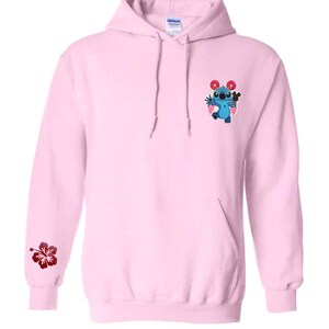 May include: Light pink hoodie with a front pocket and drawstring. Features a blue cartoon character with donuts and a hibiscus flower on the sleeve. The brand name "Yutopia Creations" is printed at the bottom.