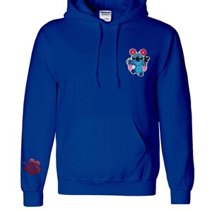 May include: Royal blue hoodie with a front pocket and drawstring hood. Features a cartoon character graphic on the chest and a red hibiscus flower on the left sleeve. The hoodie has the text "Yutopia Creations" at the bottom.