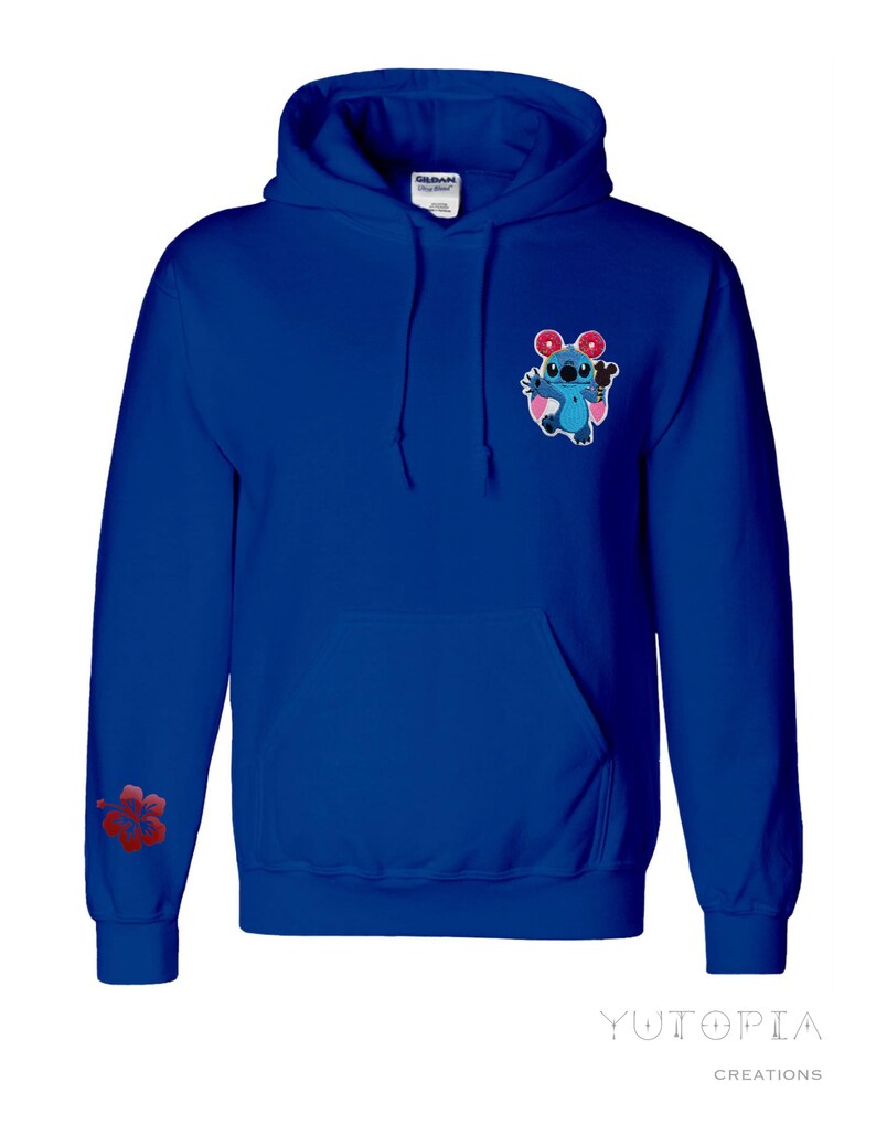 May include: Royal blue hoodie with a front pocket and drawstring hood. Features a cartoon character graphic on the chest and a red hibiscus flower on the left sleeve. The hoodie has the text "Yutopia Creations" at the bottom.