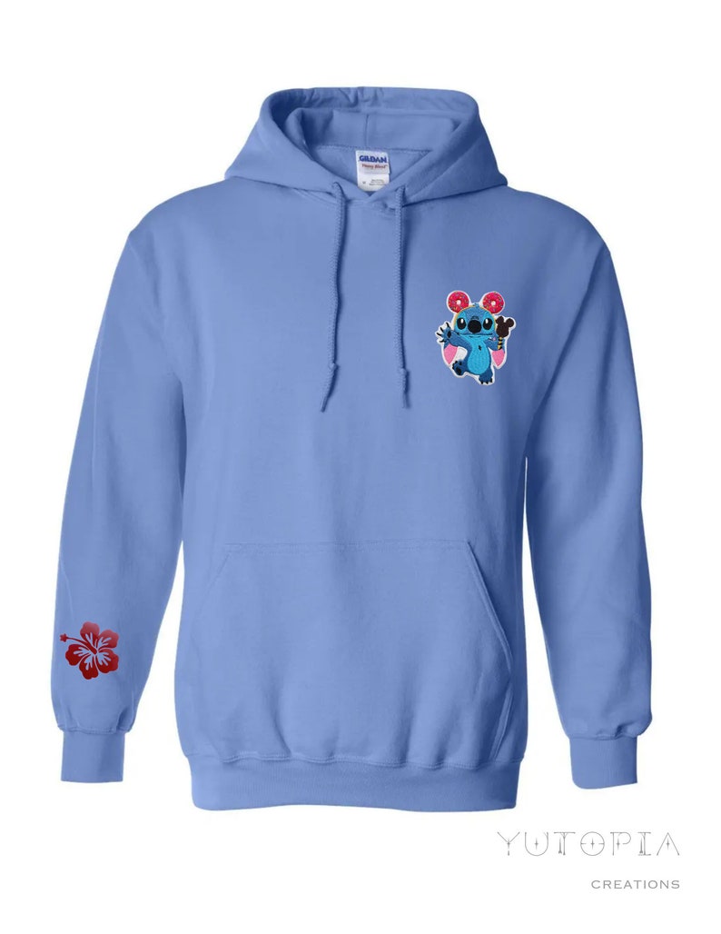 May include: A light blue hooded sweatshirt with a front pocket and drawstring. The left sleeve features a red hibiscus flower. The chest has an embroidered cartoon character holding a donut and ice cream. The brand name "Yutopia Creations" is printed at the bottom.