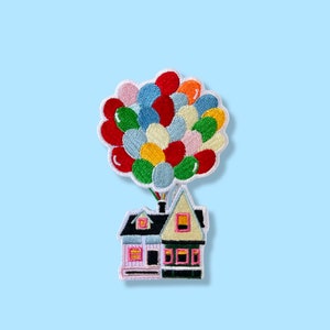 May include: Embroidered patch featuring a house lifted by a cluster of colorful balloons. The house has a light blue and beige exterior with black accents. The balloons are in various colors, including red, blue, yellow, and pink. The patch is on a light blue background.