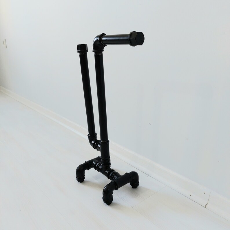 以下が含まれることがあります： 黒い金属製のパイプスタンドで、2本の垂直パイプと1本の水平パイプが上部に付いています。スタンドは4本の脚が付いたベースを持っています。