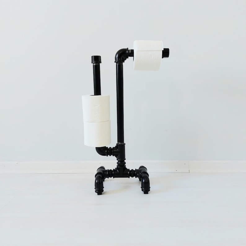 以下が含まれることがあります： 黒い金属製のトイレットペーパーホルダーにトイレットペーパーが2ロール巻かれている。ホルダーは工業用パイプで作られており、素朴な外観をしている。