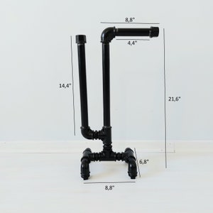 以下が含まれることがあります： U字型のデザインと4本の脚が付いた黒い金属製のトイレットペーパーホルダー。ホルダーの高さは54.9cm、幅は22.4cm、奥行きは17.3cmです。