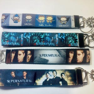 May include: Four keychains with black hardware and metal charms. The keychains feature images and text from the television show "Supernatural". One keychain has cartoon characters and the text "Hello Hunters".