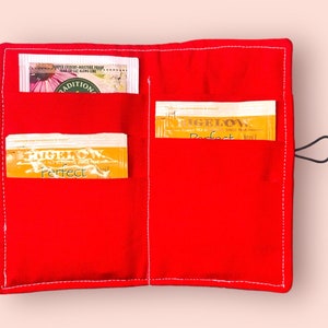 Puede incluir: Porta-bolsitas de t&eacute; de tela roja con dos bolsillos. Los bolsillos contienen bolsitas de t&eacute; con el texto "Figelow Perfect" en ellos.