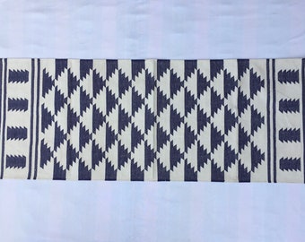Puede incluir: Una alfombra rectangular con un patrón geométrico. La alfombra presenta un diseño de diamantes repetidos en azul marino y crema. Los bordes tienen un borde azul marino con flecos en cada extremo. Adecuada para un pasillo o entrada.