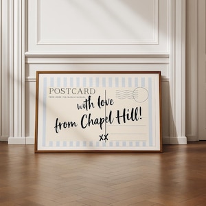 Könnte beinhalten: Ein gerahmter Postkarten-Druck mit einem braunen Holzrahmen. Die Postkarte hat einen cremefarbenen Hintergrund mit hellblauen vertikalen Streifen und den Worten "POSTCARD" und "with love from Chapel Hill!" in schwarzer Schrift.