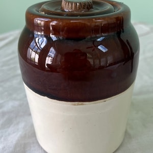 May include: A brown and white ceramic jar with a lid. The jar has a brown glaze on the top half and a white glaze on the bottom half. The lid has a brown knob.