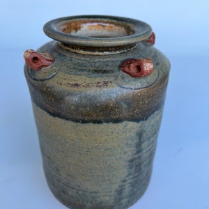 May include: A brown and gray ceramic vase with a wide mouth and three small handles. The vase has a rustic, handmade look.