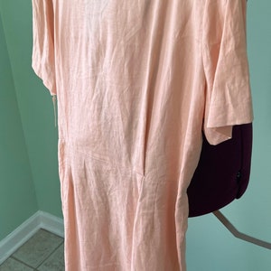May include: A peach-colored linen dress with short sleeves and a V-neckline. The dress has a fitted bodice and a flowy skirt.