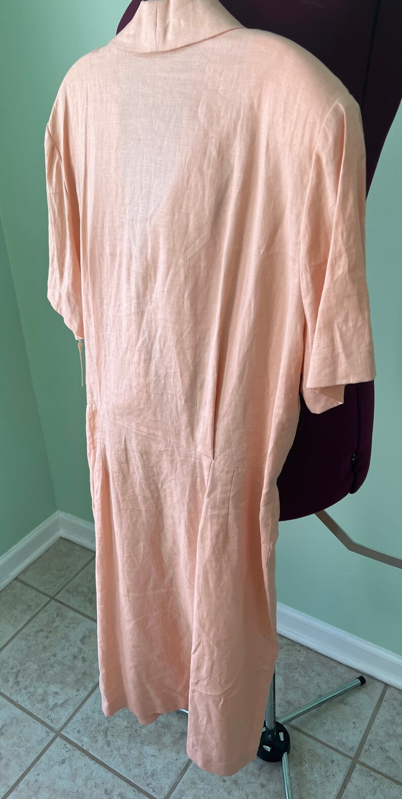May include: A peach-colored linen dress with short sleeves and a V-neckline. The dress has a fitted bodice and a flowy skirt.