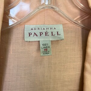 May include: A light pink linen shirt with a white tag that reads "Adrianna Papell 100% Linen 16 Made in Korea."