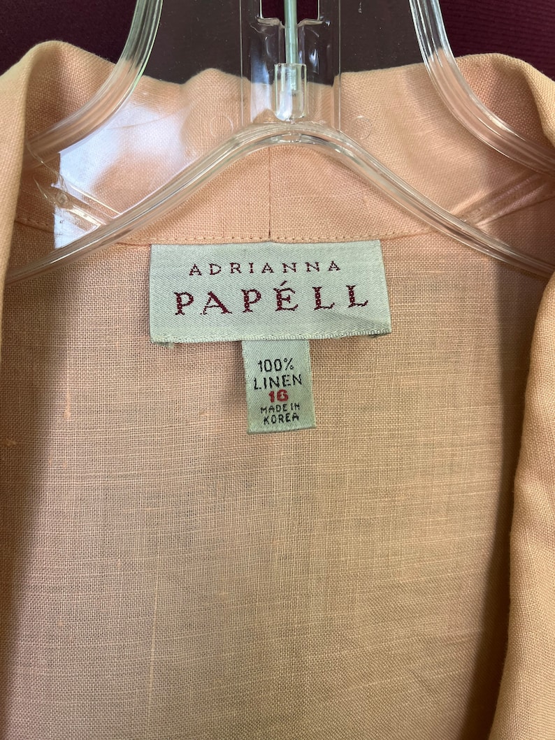May include: A light pink linen shirt with a white tag that reads "Adrianna Papell 100% Linen 16 Made in Korea."