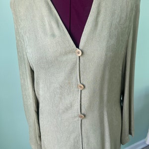 May include: A light green long-sleeved button-up shirt with a V-neck and a subtle pattern. The shirt has four brown buttons down the front.