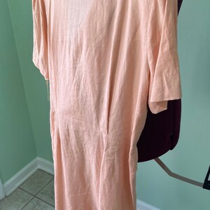 May include: A peach-colored linen dress with short sleeves and a V-neckline. The dress is fitted and has a flowy skirt.