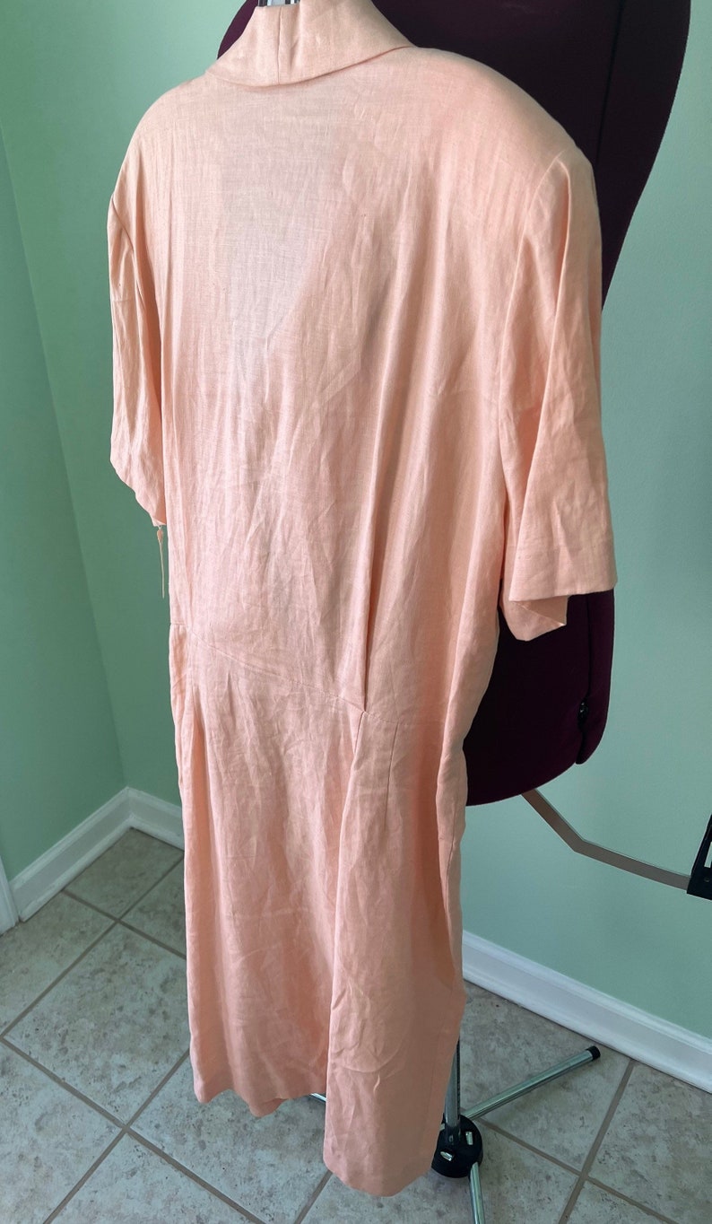 May include: A peach-colored linen dress with short sleeves and a V-neckline. The dress is fitted and has a flowy skirt.