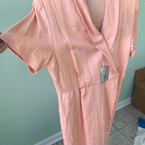 May include: A peach-colored linen dress with a wrap-style neckline and short sleeves. The dress has a tag that reads "Adriana Papell".