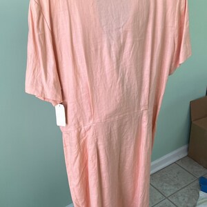 May include: A peach-colored linen dress with a collared neckline and short sleeves. The dress has a button-up front and a fitted waist.