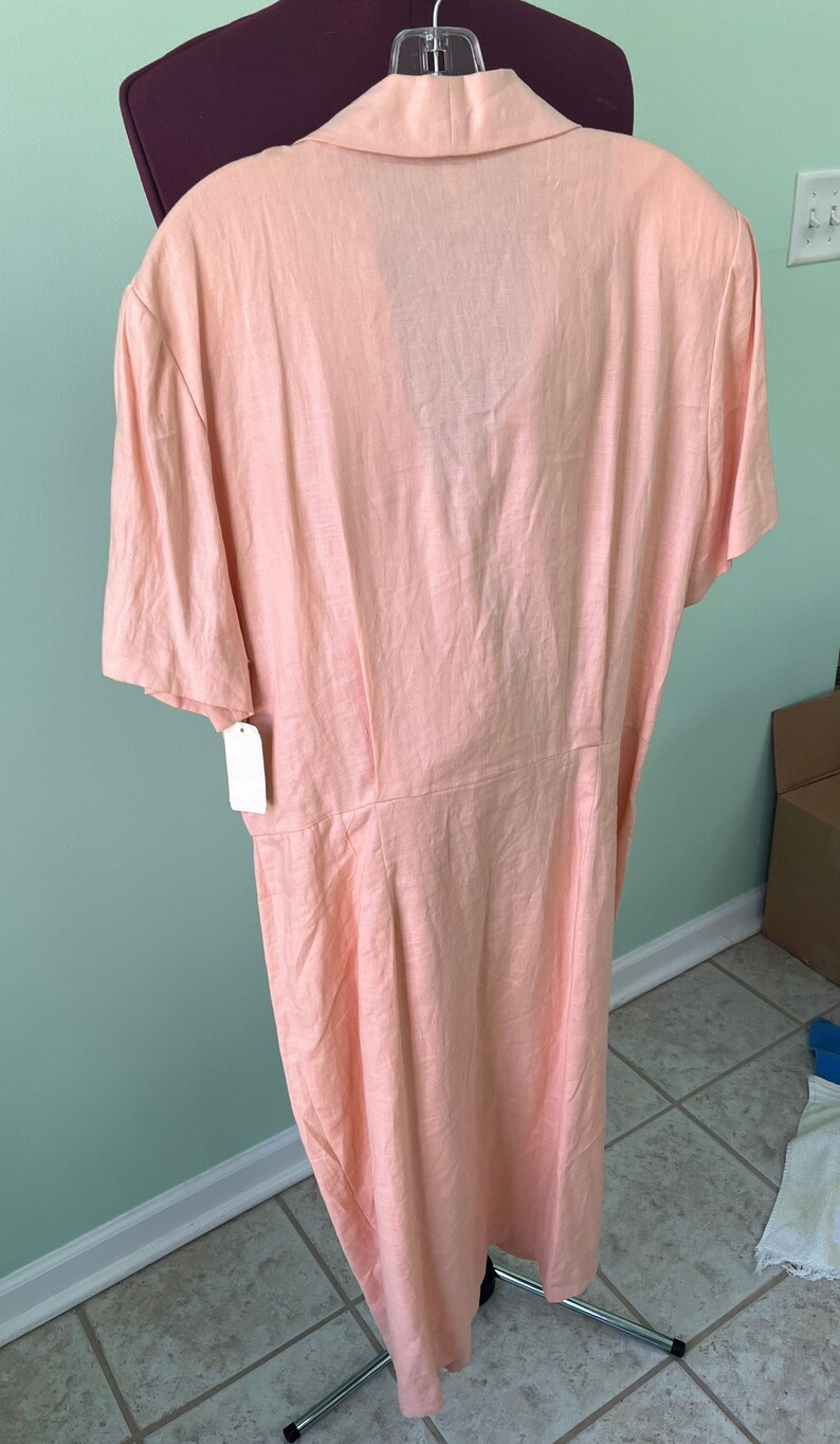 May include: A peach-colored linen dress with a collared neckline and short sleeves. The dress has a button-up front and a fitted waist.