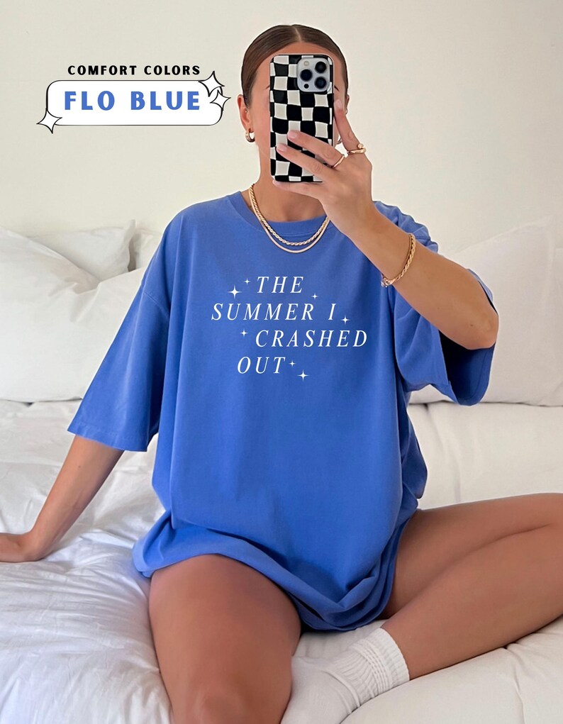 Pode incluir: Uma camiseta azul com o texto "THE SUMMER I CRASHED OUT" em branco. A camiseta &eacute; de cor confort&aacute;vel e a cor &eacute; "FLO BLUE". A imagem tamb&eacute;m mostra uma pessoa usando a camiseta.